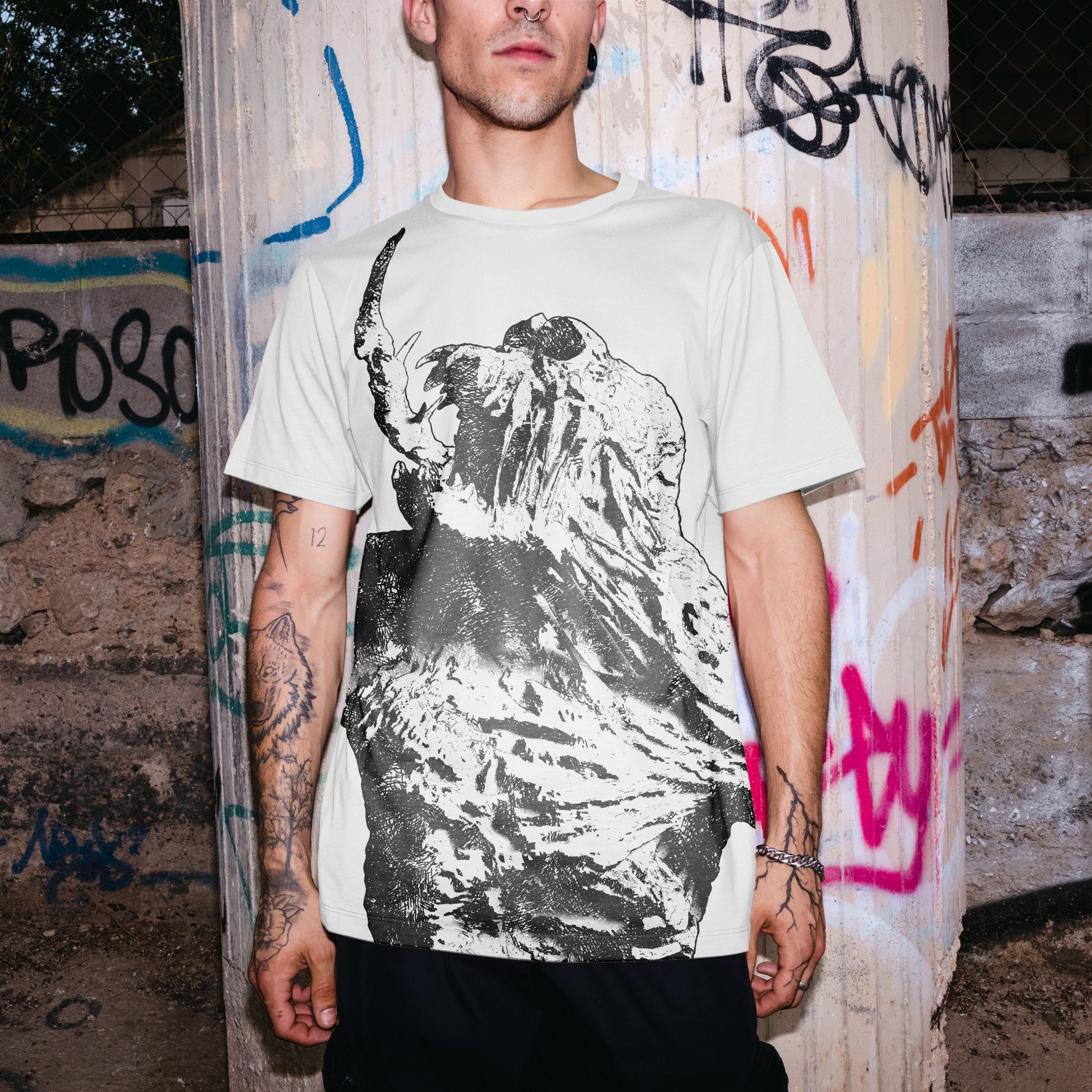 Man wearing a graphic t-shirt standing in front of a graffiti-covered wall.